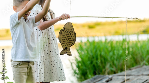 Tableau sur toile Children pretend fishing with a cardboard fish and a stick by the water
