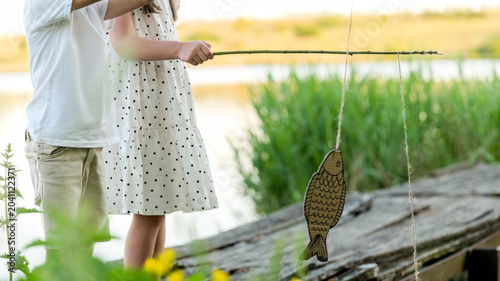 Tableau sur toile Children pretend fishing with a handmade fish on a stick by the water
