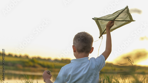 Canvas Print Boy holding a homemade kite against a bright sky at sunset
