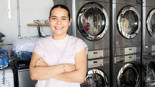 Foto Portrait of a smiling young woman standing confidently inside a modern laundromat, with industrial front-loading washing machines in the background