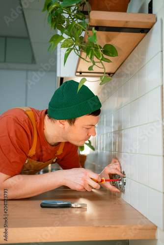 Electrician providing professional handyman service installing an electrical wall socket, using a screwdriver to connect wires for a home improvement project or small craft business order