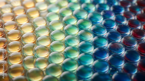 Closeup of a colorful array of smooth, translucent glass pebbles arranged in a gradient pattern, transitioning from warm yellow and orange to cool green, blue, and deep red tones