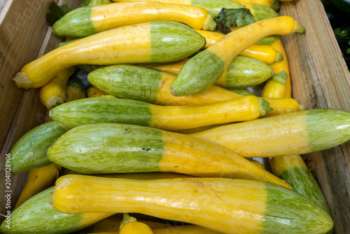 A close-up of a wooden crate filled with fresh bicolour yellow and green courgettes on display at a market stall