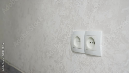 Electrical cord removal process. Carefully disconnecting wire from socket with attention. Closeup shot capturing safe unhooking of electrical cord adjacent to textured wallpaper and baseboard