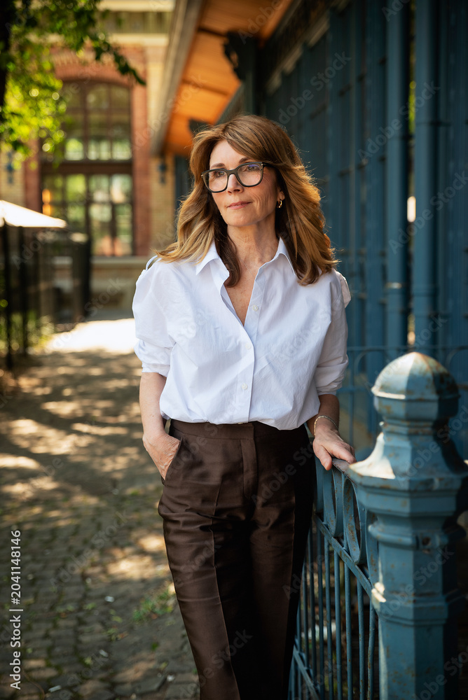 Fototapeta premium Confident mature business woman standing in doorway wearing white shirt and glasses