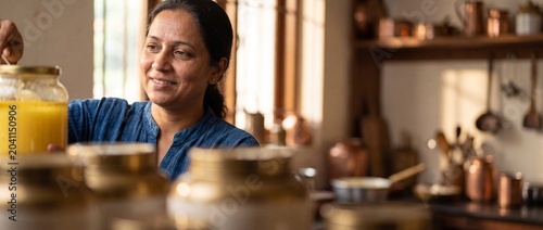 Indian woman cooking organic ghee in rustic kitchen lifestyle, smiling happy female chef preparing healthy homemade clarified butter culinary ingredient in traditional warm home cozy food environment.