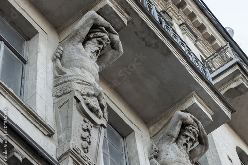 Obraz na plátně Weathered stone atlantes support a balcony on a historic building facade, showing classical muscular figures and intricate masonry details that convey age, craftsmanship and heritage of St