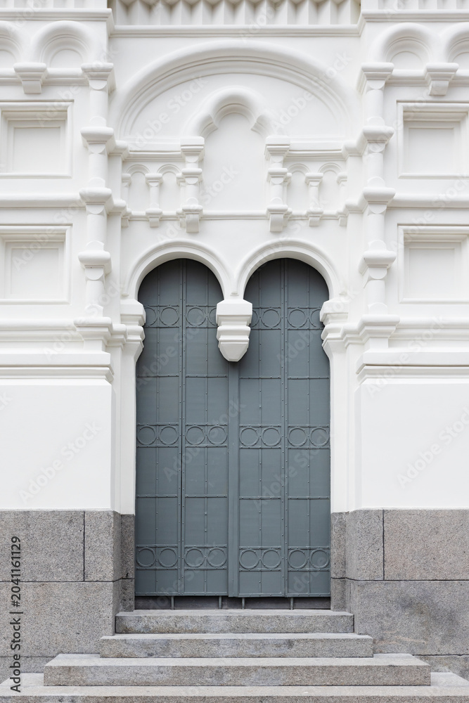 Obraz premium Elegant arched double door set into a white, ornate classical Church facade with decorative moldings and granite steps; minimal, symmetrical architectural detail conveying history calm