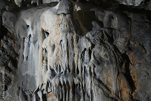 Massive stalactite formations and vertical cave drapery on a textured limestone wall.