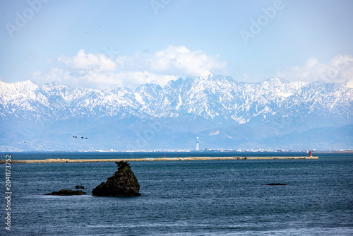 雨晴海岸の青い海原の向こうに、冠雪した雄大な立山連峰がそびえ立つ絶景