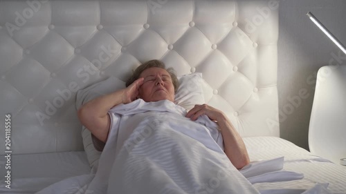 An elderly woman can't sleep because of the noise from her neighbors and covers her head with a blanket