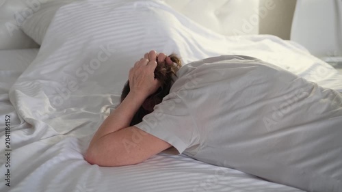 An elderly woman cries hysterically on her bed, clutching her hair