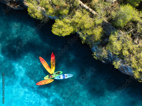 Canvastavla Aerial drone view of colorful kayaks in crystal clear turquoise sea near rocky coast and green trees