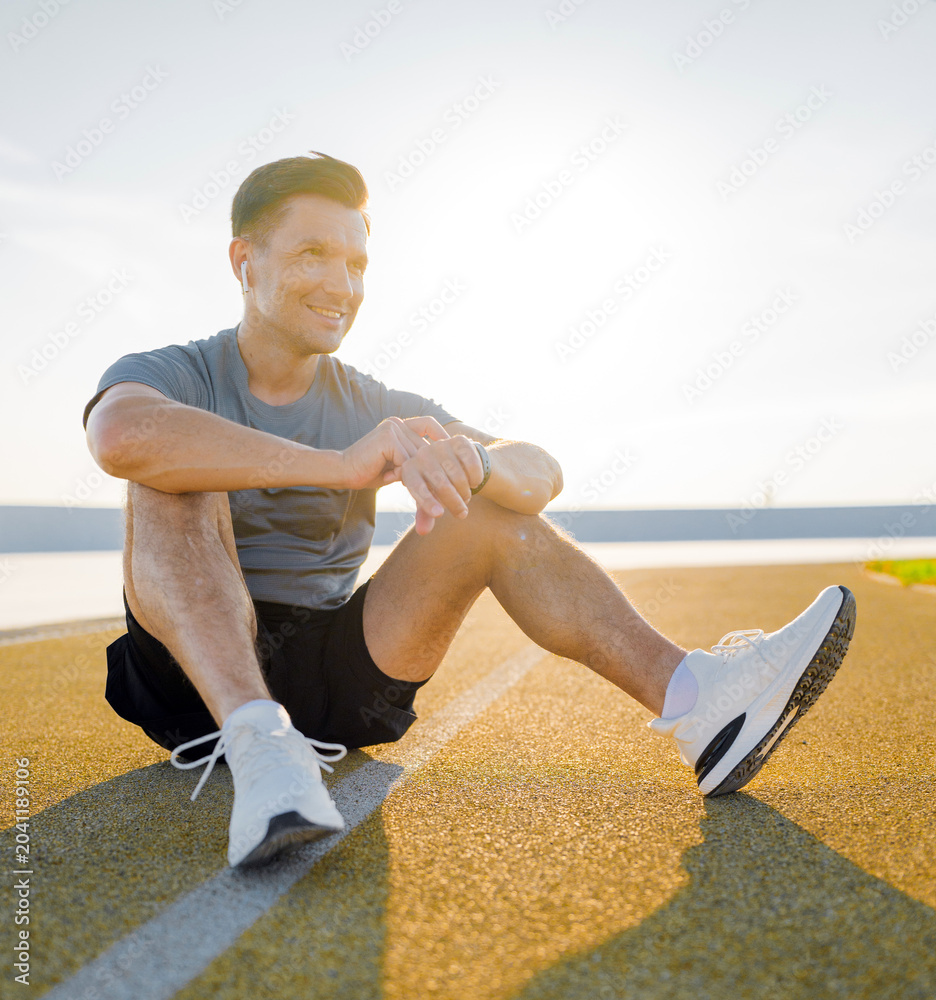 Fototapeta premium Athletic man relaxing on a sunny track after a workout in a vibrant outdoor setting