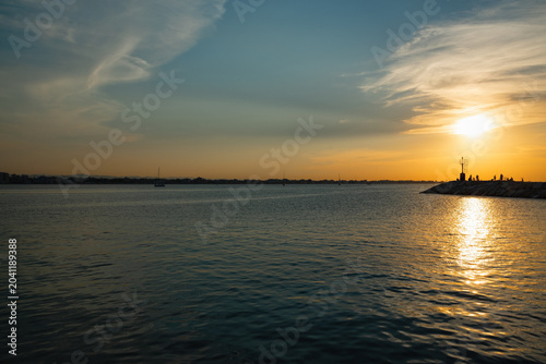 Sunset over water with silhouettes of people enjoying the view at a coastal location