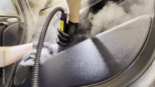 Dry cleaning of the car leather interior, car door trim using a special brush. The detailing master cleans the car interior with a hot steam cleaner, brush, microfiber. Concept of car interior care.