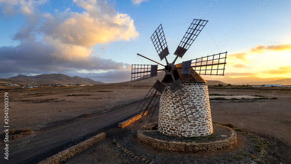 Obraz premium Cinematic drone shot of old Tefia windmill in deserted Spanish landscape at sunset, Fuerteventura, Canary Islands Wild volcanic scenery. authentic Spain, wall art print .copy space sky