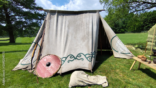 Foto Medieval Viking tent with traditional patterns, round wooden shield, and bow at historical reenactment camp on green grass