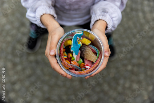 Child's hands holding a cup full of colorful gummy candies.