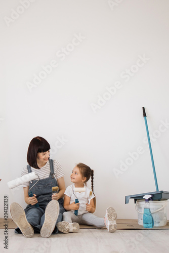 Slika na platnu A mother and her young daughter sit on the floor, holding paint rollers and brus