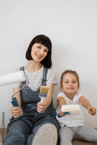 Foto A smiling mother and her young daughter sit together holding painting tools, rea
