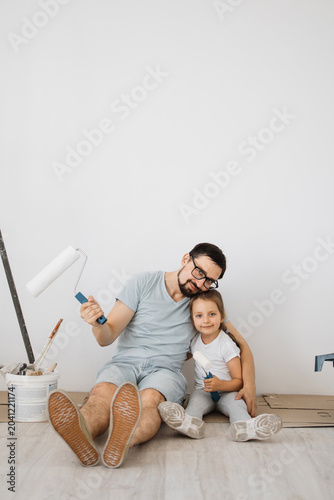 Obraz na płótnie A father and his young daughter sit on the floor, smiling and holding paint roll
