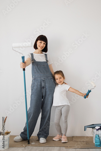 Fotografía A smiling mother and her young daughter stand side-by-side, holding paint roller