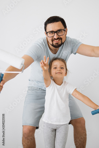 Tablou pe pânză A smiling father and his young daughter playfully hold a paint roller, ready to