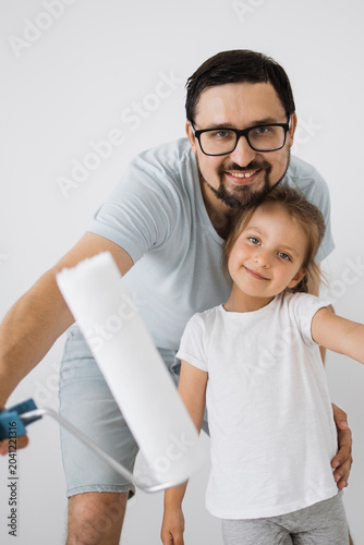 Photos A father and his young daughter smile while holding a paint roller, ready to red