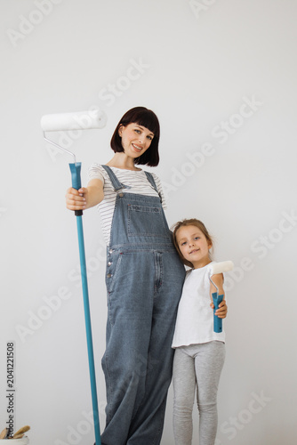 Foto A woman and a young girl in overalls stand side-by-side holding paint rollers, r