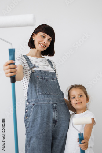 Tableau sur toile A woman and a young girl in denim overalls smile while holding paint rollers, re