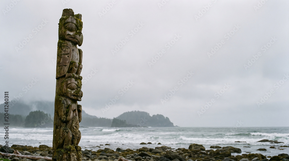 Obraz premium Ancient carved totem pole stands sentinel on a rugged Canadian coastline, a powerful cultural symbol against the dramatic misty landscapes
