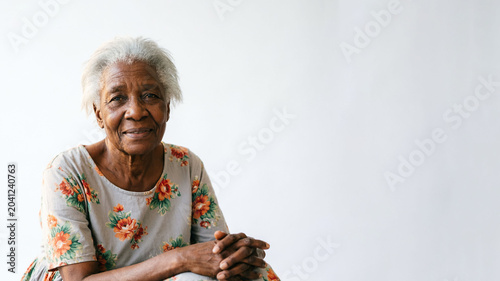 An old African American pensive woman wearing a flowered house dresson a white background (copy space)