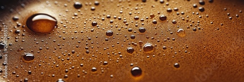 Close-up of a smooth surface with droplets reflecting light, showing rich golden brown hues of liquid at moderate ambient lighting