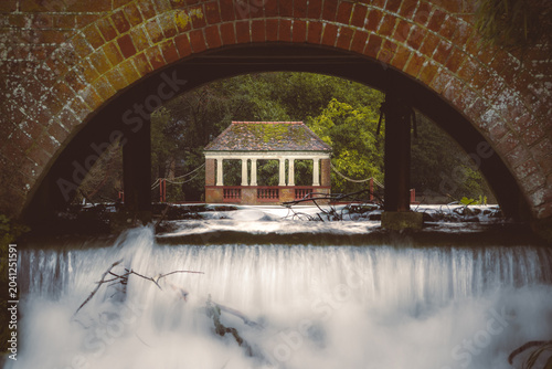 Waterfall Framed by Brick Arch with Classical Pavilion Beyond