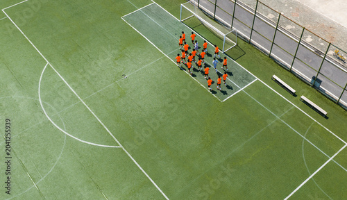 Fotografie Aerial view of children in orange jerseys running across the soccer field during soccer practice at a sports park in Wuhan, China