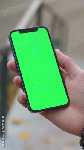 Hand with phone, Detailed view of person holding smartphone with green screen and seasonal outdoor surroundings