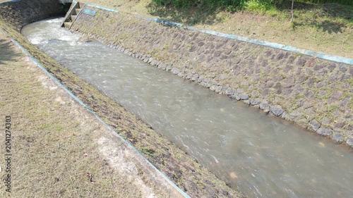 A tranquil scene of a meandering waterway lined with grassy banks and textured stone edges under bright daylight