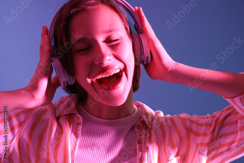 Young woman in headphones listening to music on purple background, closeup