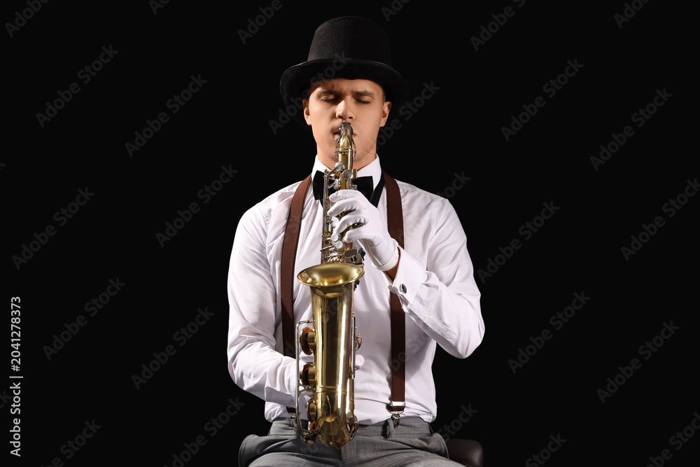 Fototapeta premium Male artist playing saxophone on black background
