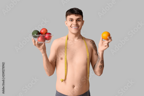 Young man with fruits and measuring tape on grey background. Weight loss concept