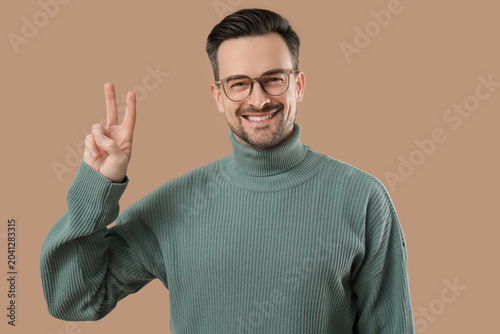 фотографія Handsome young man in eyeglasses showing victory gesture on brown background