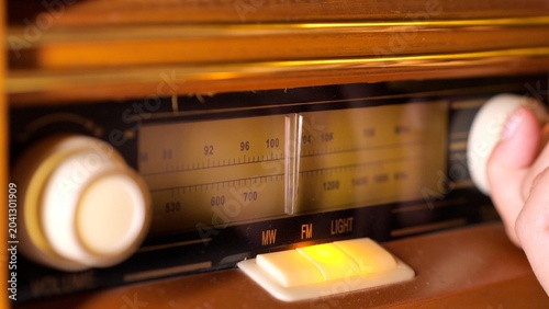 Bild auf Leinwand Hand adjusting the dial of an old wooden radio, searching for a specific frequen