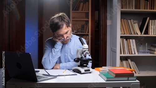 Konstfotografi Young man wearing glasses is falling asleep at his desk, exhausted from long hou