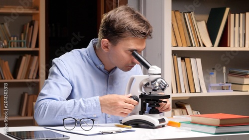 Фотография Young male researcher closely examining a sample under a microscope at a desk in