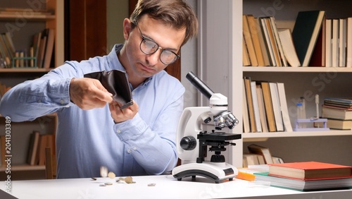 Obraz na plátně Researcher at a cluttered desk with microscope and books, holding an empty walle