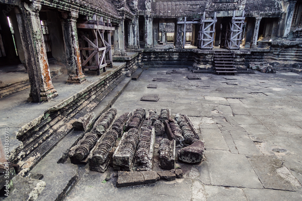 Fototapeta premium Ancient stone carvings lie scattered in the courtyard of Angkor Wat temple complex in Siem Reap, Cambodia. The temple is a UNESCO World Heritage site.