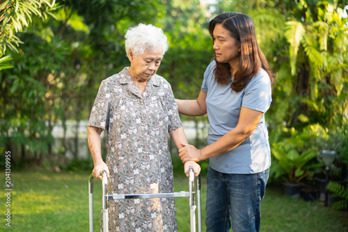 Caregiver help Asian elderly woman patient walk with walker in park.