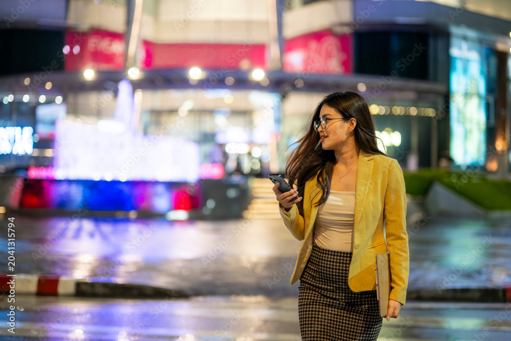 Fototapeta premium Businesswoman walking and using smartphone in city at night