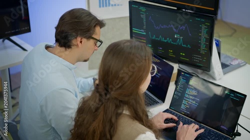 Female data scientist and male software engineer reviewing live machine learning training dashboard and GPU monitoring on screen. Artificial intelligence research, data analysis, technology workspace.